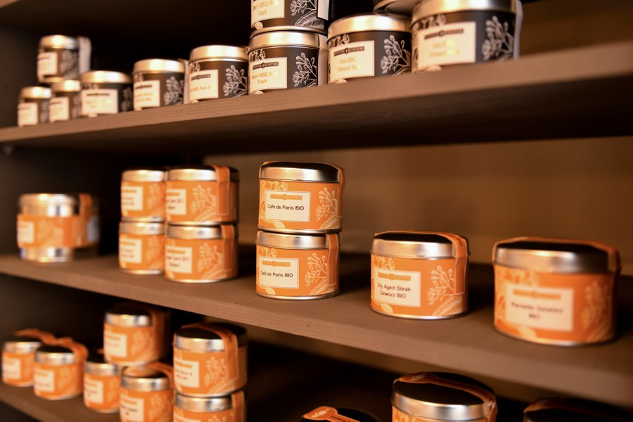 Holzregal mit mehreren runden Gewürzdosen, ordentlich nebeneinander platziert, im Fokus stehen drei Dosen in der vorderen Reihe.