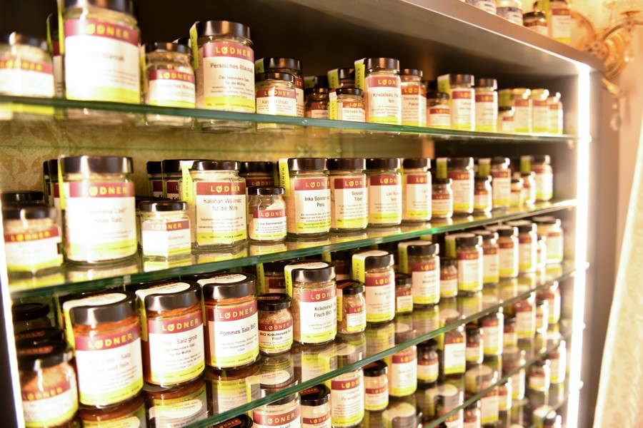 Mehrere Regalböden voller Gewürzgläser mit einheitlich gestalteten Etiketten in einer übersichtlichen Anordnung.