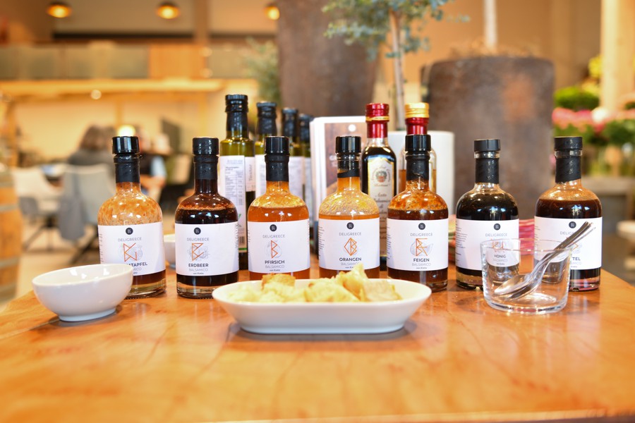 Feinkostprodukte wie Öle, Essige und Pasta, ansprechend präsentiert auf einem Holztisch mit kleinen Probierportionen.