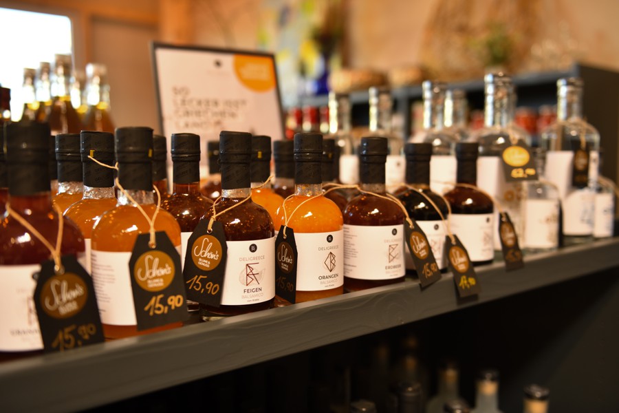Nahaufnahme eines Regals mit Flaschen regionaler Essig- und Öl-Spezialitäten, mit Preisschildern.
